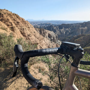 Gravel bike handlebars in the foreground with a canyon and Badlands landscape in the distance, part of a scenic gravel bike ride on Hidden Tracks Cycling's Flamenco Gravel trip.