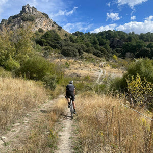 Gravel cyclist riding along a rough track through scrubland with mountains in the background, part of a guided bike adventure on Hidden Tracks Cycling's Flamenco Gravel trip in spring