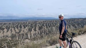 Gravel cyclist standing on a scenic overlook with a vast landscape in the background
