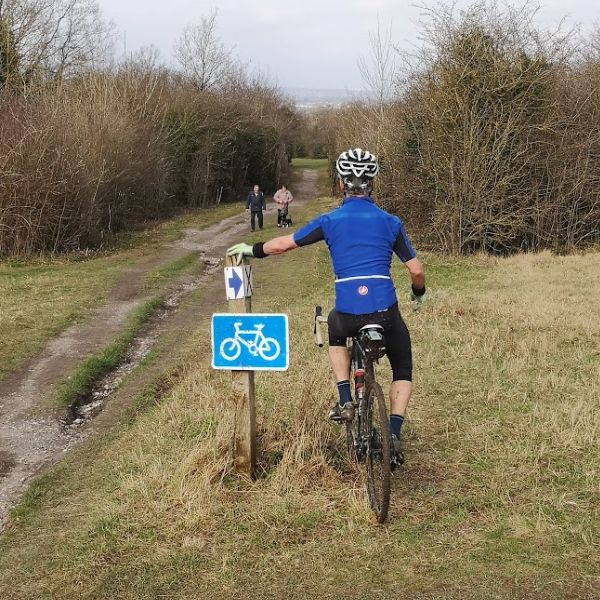 Gravel cyclist leaning against a clue bike route sign near Epsom