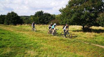 Group of 4 mountain riders riding across a field with trees in the background 