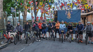 A group of cyclists lined up with their bikes outside the Trafalgar Tavern, surrounded by colourful nautical flags, preparing to begin the 360 Gravel event.