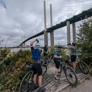 Group of gravel cyclists riding from London to Paris, stopping to admire the Queen Elizabeth Bridge at Dartford with the Thames in the background on Hidden tracks Cycling's ride from London to Paris.