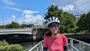 Cyclist standing on a bridge over a river with trees and blue sky in the background during the 360 Gravel event.