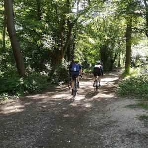 Gravel cyclists charging along Pilgrims Ways through a sunlit wood in Summer, typically found on one of Hidden Tracks Cycling's Gravel rides 