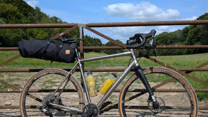 Bicycle with gear leaning against a a gate, with a wooded landscape in the back ground 
