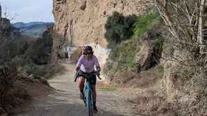 Gravel rider  riding a bicycle on a dirt trail with rocky cliffs and sparse vegetation on the Badlands Gravels Training Camp 
