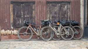 Dusty laden gravel bikes leaning against and old wooden wall with peeling purple paint, seen on Hidden Tracks Cycling's Trail of 2 Cities ride from London to Paris 