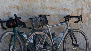 Two gravel bikes with gear packs and water bottles against a stone wall.