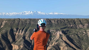 Gravel cyclist  helmet and orange shirt standing on a cliff overlooking a scenic landscape across to the snow capped Sierra Nevada mountains 