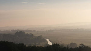 A cold grey Dawn on a Summers morning, show mist in the valley with a small river as discovered on Hidden Tracks Cycling's The Wrecker ride 