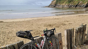 A fully loaded gravel bike leaning against a wooden fence with the sea shore in the background 
