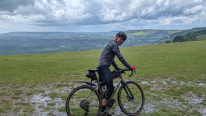 Cyclist paused on a muddy gravel bike with wide rolling hills and cloudy skies during the 360 Gravel ride.