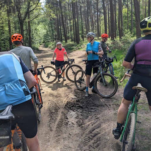 Bunch of Gravel cyclists taking a break in the sunlit woods in Summer 