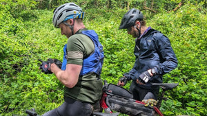 Two cyclists stopped in dense green woodland checking navigation devices during the 360 Gravel event.