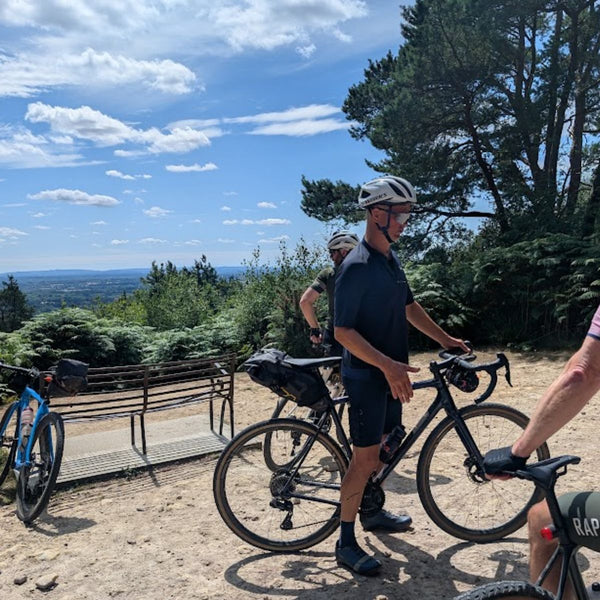 Bikepackers with loaded gravel bikes resting at a viewpoint bench overlooking the Weald on the Brighton Bound route.