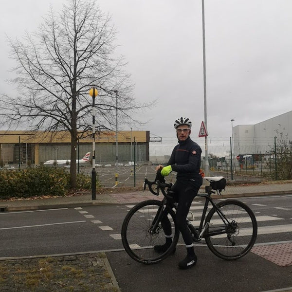 A cyclist beside the Heathrow perimeter road on this gravel bike route from London, with a plane parked just behind the fence