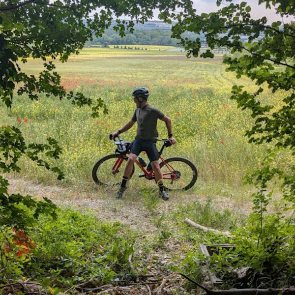 Gravel cyclist with a red bike at the edge of a poppy and wildflower field, framed by trees, on The Runaway King route to Faversham.