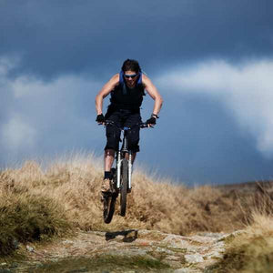 Mountain bike rider cycling down a rocky path against a dark sky 