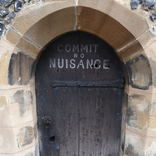 Arched shape ancient black wooden door t with ‘Commit no nuisance ‘ written on it in white paint as seen on Hidden Tracks Cycling’s Pilgrimage to St Albans Gravel bike route