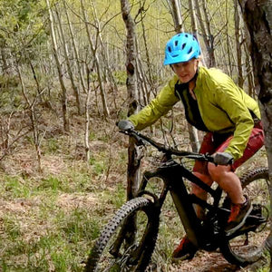 Woman cyclist on an electric mountain bike riding a trail through the woods 